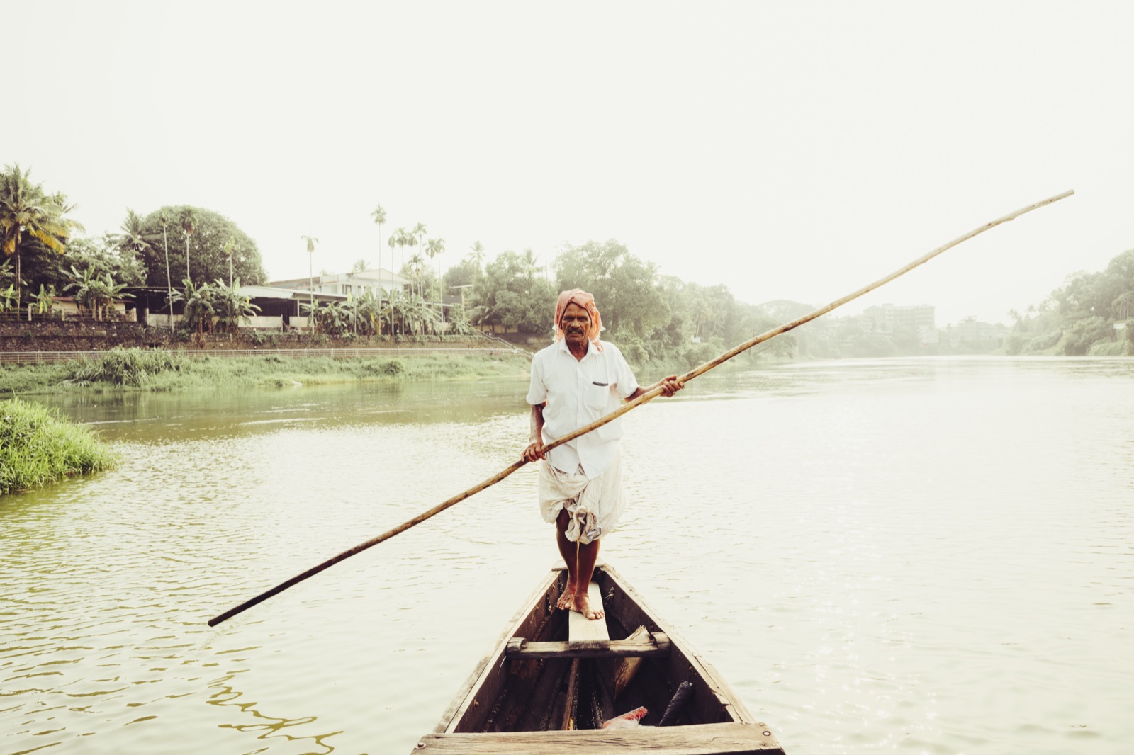 A boatman poling a country canoe across the river