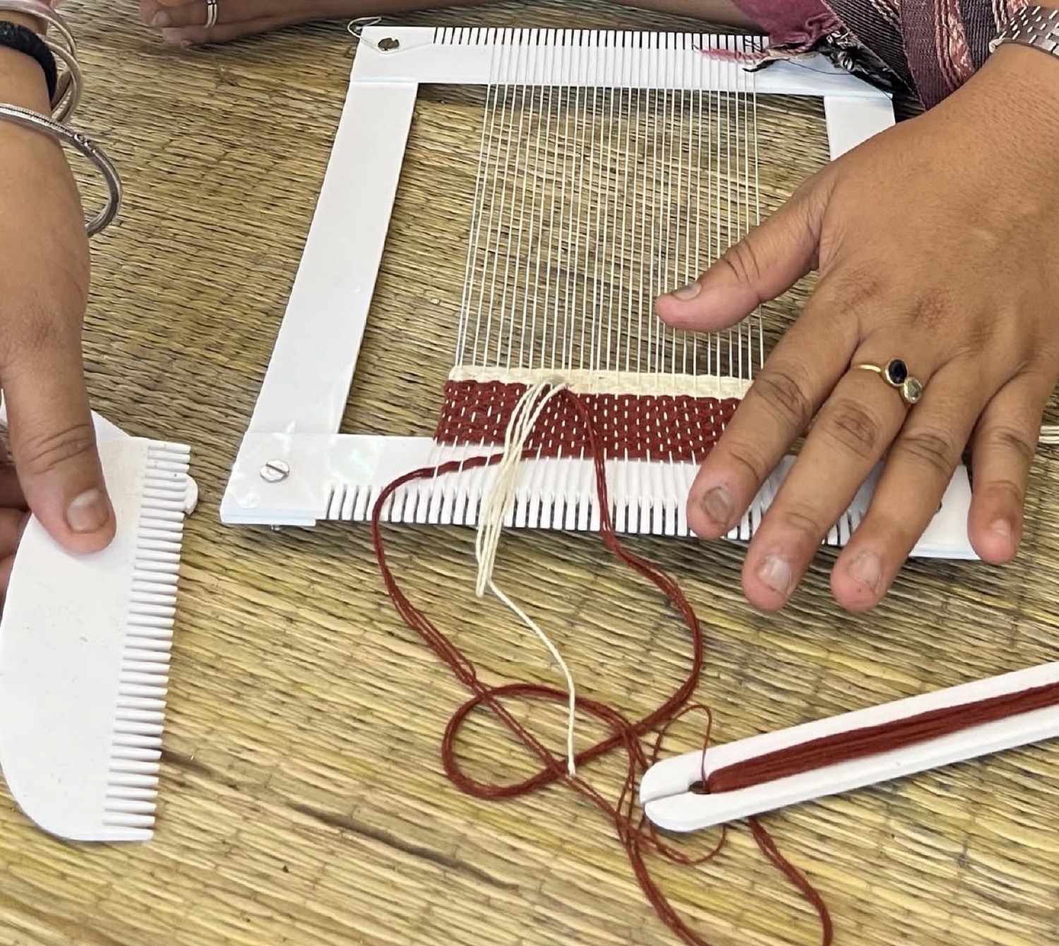 Hands weaving a small tapestry on a frame loom