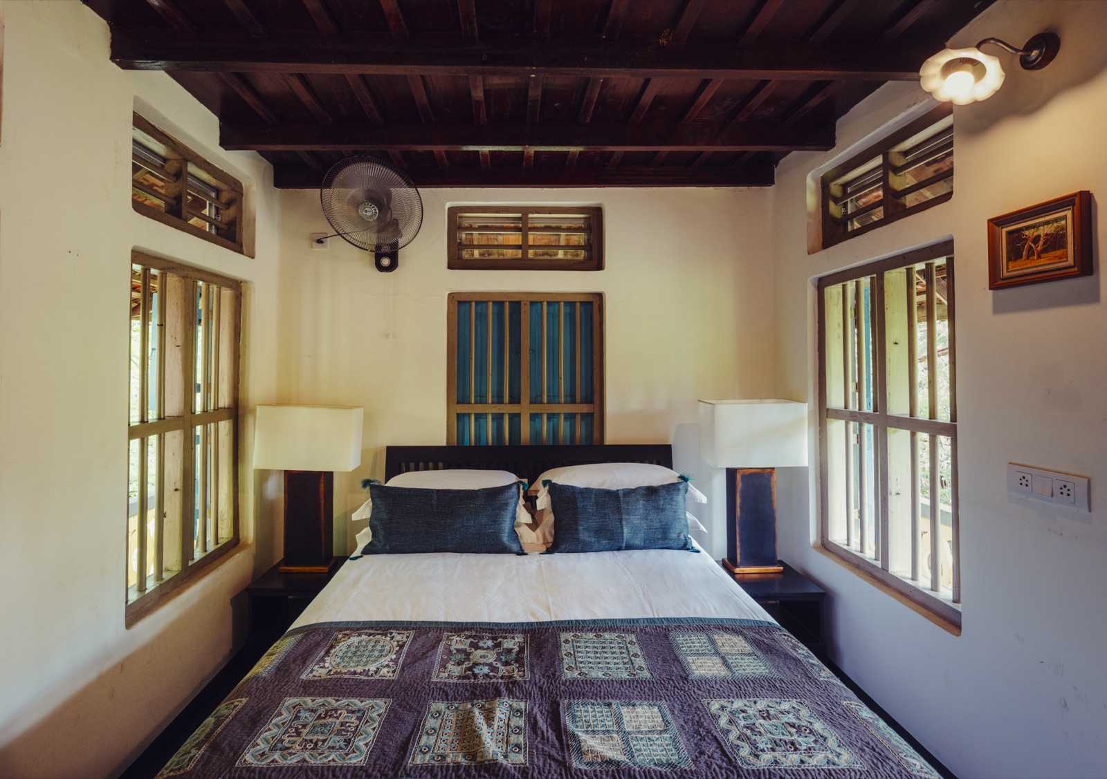 The Radha bedroom — a king bed below a timber ceiling, with blue-shuttered windows