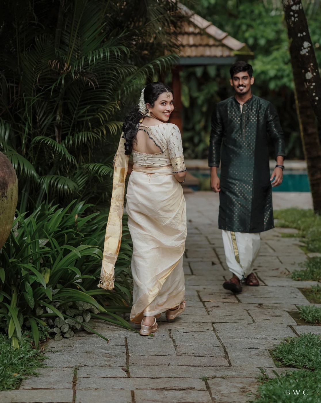 A bride in a cream kasavu saree and groom in the estate garden
