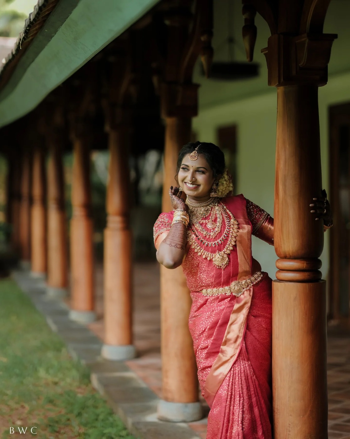 A bride in a red kasavu saree in a doorway of the house