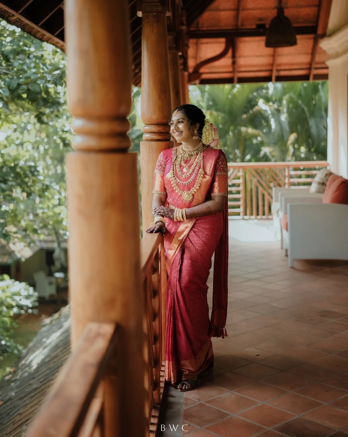 A bride in a red kasavu saree against the estate's carved timber columns